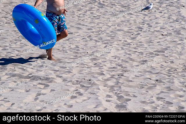04 September 2023, Mecklenburg-Western Pomerania, Zinnowitz: A vacationer walks across the beach with a swimming ring in sunny weather