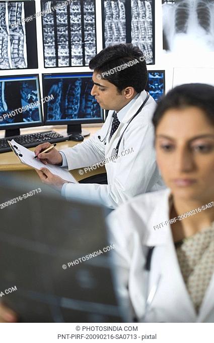 Female doctor examining X-Ray report and her colleague writing prescription