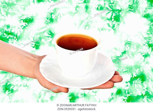 White teacup with saucer in hand on abstract plant background