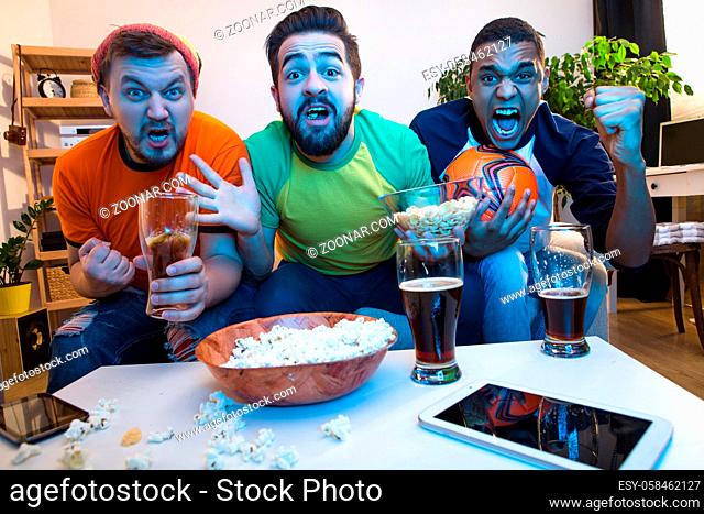 Picture of funny friends watching football game on TV, drinking alcohol drinks and screaming or shouting while catching exciting or amazing moments