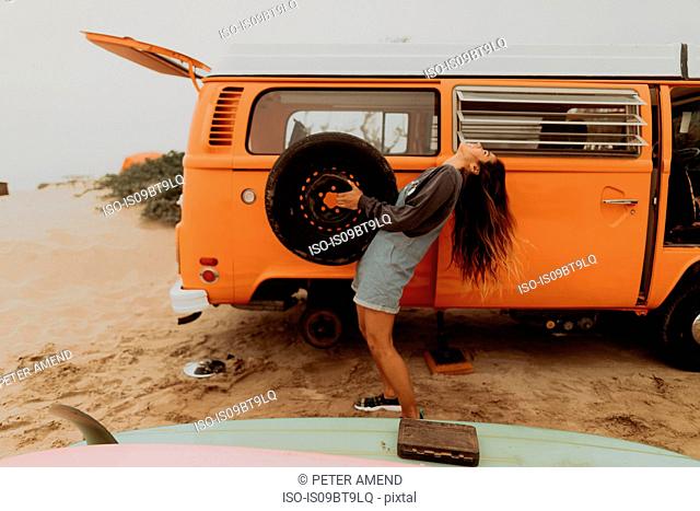 Young woman holding up recreational vehicle tyre at beach, Jalama, California, USA