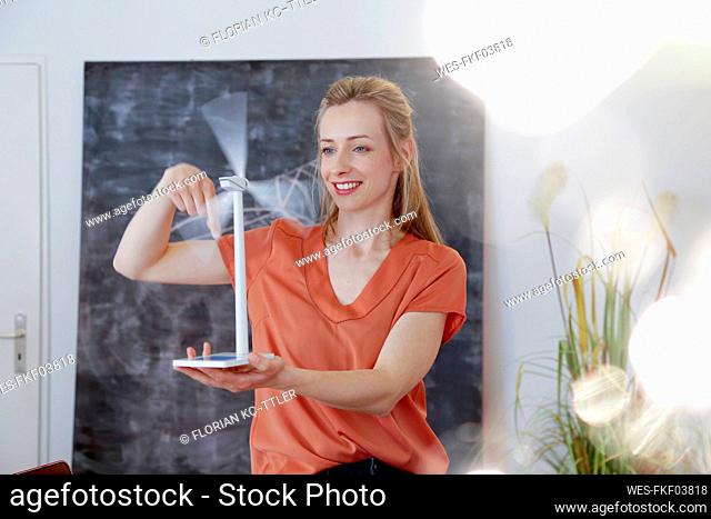 Smiling woman in office rotating wind turbine model