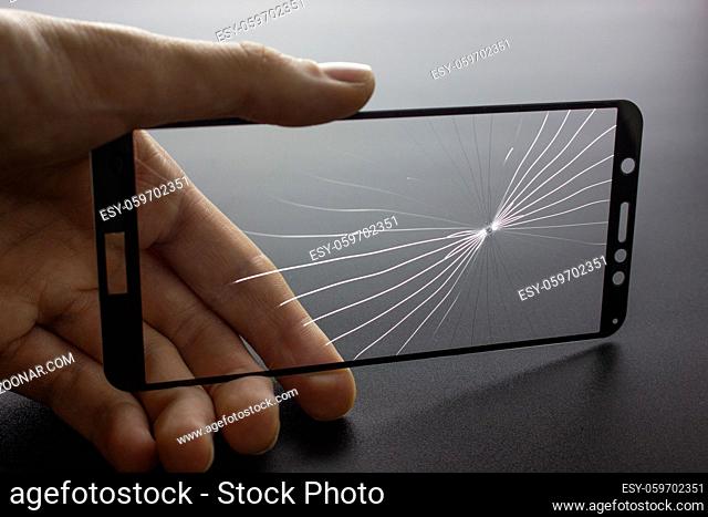 Broken protective glass of smartphone with cracks in hand on black background. Broken glass protection smartphone