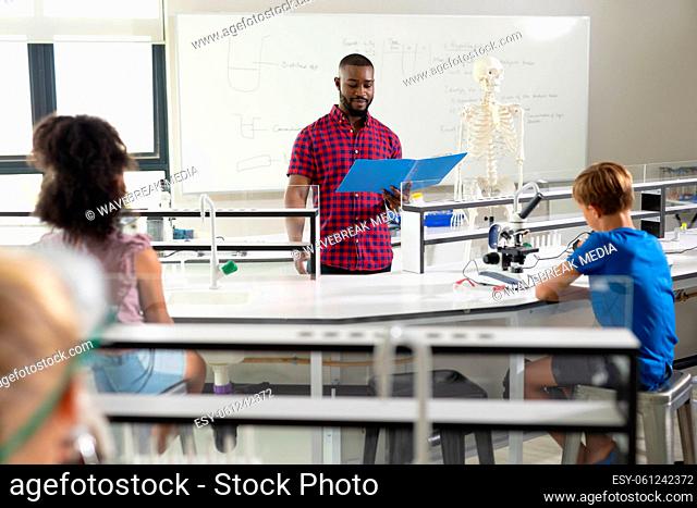 African american young male teacher reading notes to multiracial elementary students in laboratory