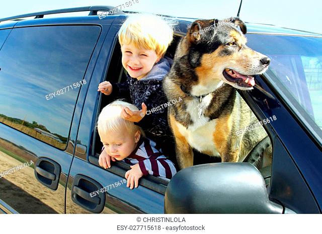 wo happy young children and their German Shepherd dog are hanging out the window of a minivan