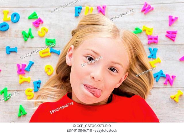 Cheeky little girl. Top view of cute little girl grimacing while lying on the floor with plastic colorful letters laying around her
