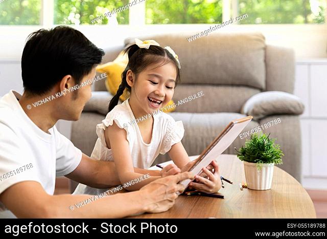 Asian girl reading tale story book with her father in living room while city lockdown from coronavirus covid-19 pandemic