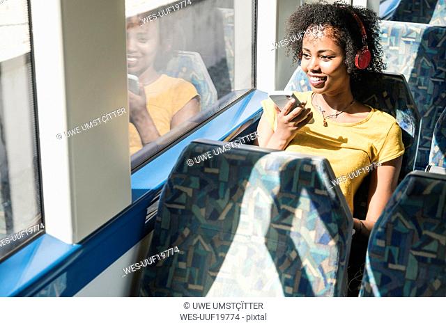 Smiling young woman with headphones and smartphone on a train