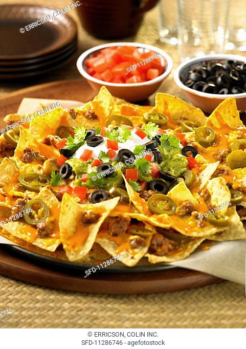 A nacho platter with guacamole, cheese and jalapeños