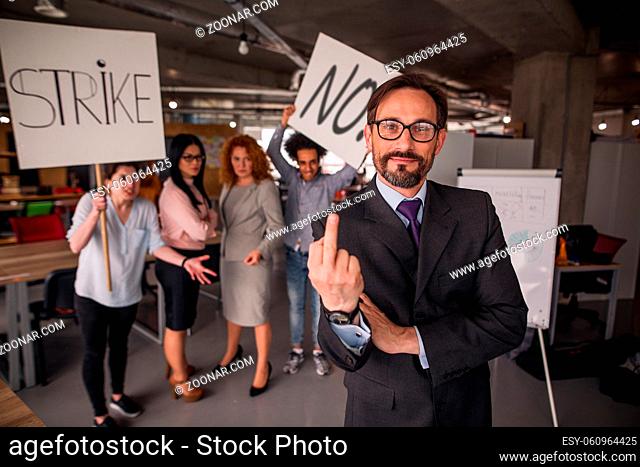 Happy director in loft office showing long finger to camera, striking workers behind him. Modern office in loft style, unhappy employees