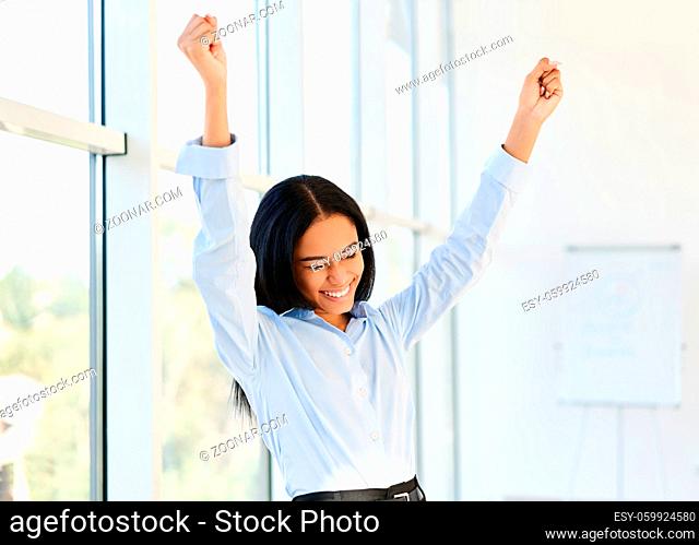 Portrait of happy excited black businesswoman with arms raised celebrating success in modern creative office