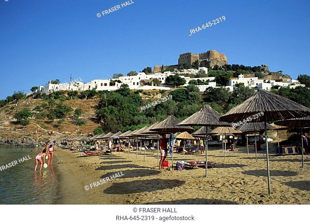 The beach below the white houses and acropolis of Lindos Town, Rhodes, Dodecanese Islands, Greek Islands, Greece, Europe