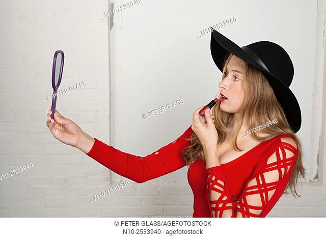 Blonde teenage girl holding a mirror and applying lipstick