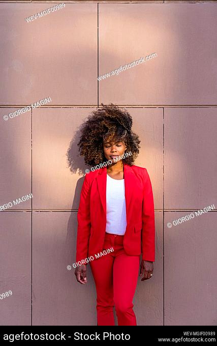 Woman with eyes close standing against brown wall