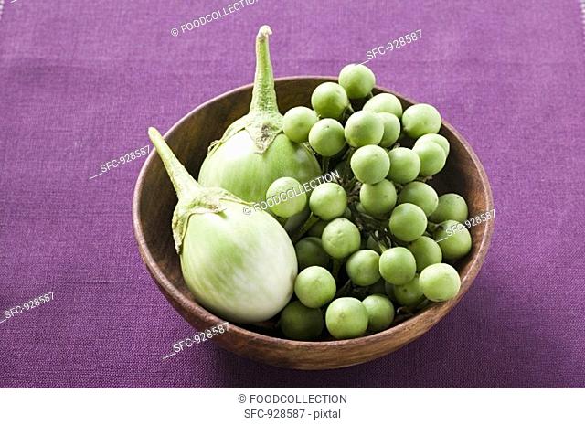 Green baby aubergines in wooden bowl