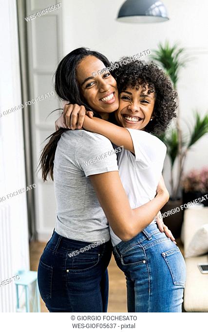 Portrait of two happy girlfriends hugging at home
