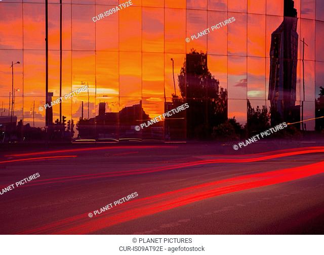 Highway traffic light trails and glass fronted office building at sunset