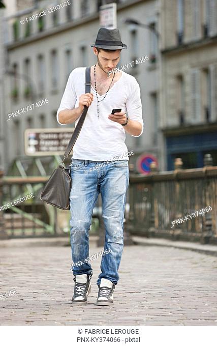 Man walking on the road and text messaging with a mobile phone, Paris, Ile-de-France, France