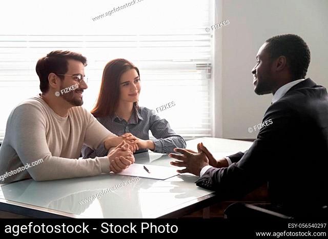 Smiling african american male banker lawyer real estate agent consulting young married couple. Satisfied clients discussing contract insurance details with...