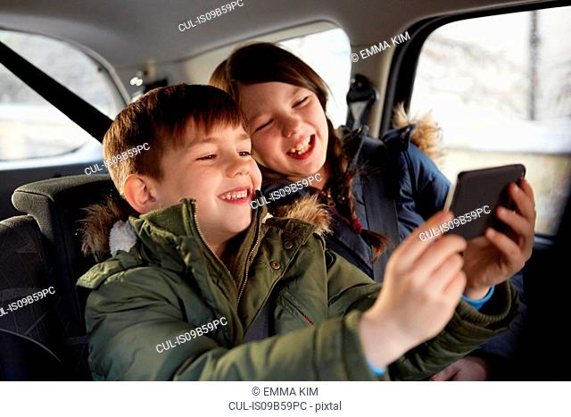 Boy and sister taking laughing selfie in car backseat