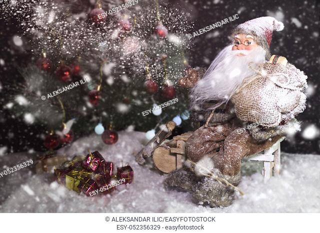 Santa Claus Outdoors Beside Christmas Tree in Snowfall Carrying Gifts to Children. Merry Christmas & New Year's Eve concept