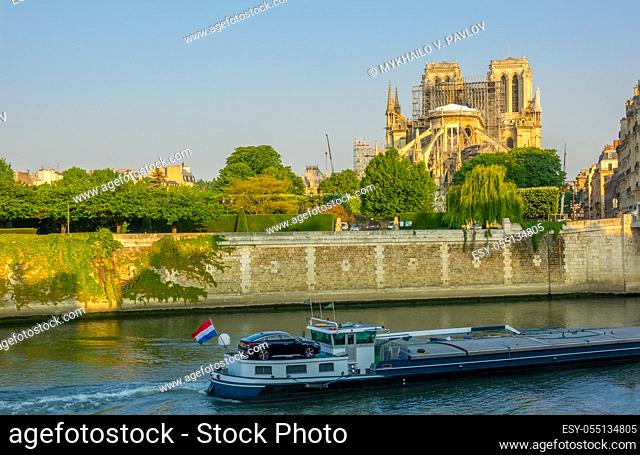 France. Paris. Sunny summer morning on the Seine embankment. Notre Dame in scaffolding after a fire in 2019. Barge on the river