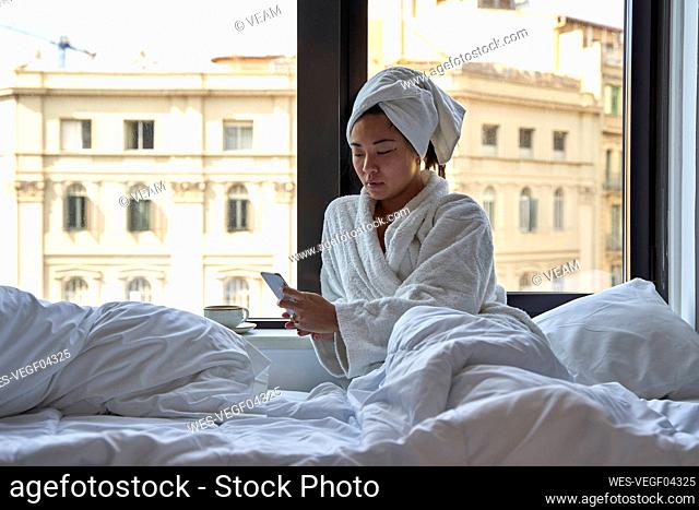 Young woman using smart phone while sitting on bed of hotel