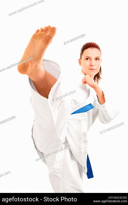 A portrait of a beautiful young girl in a kimono with blue belt demonstrating a kick, isolated on white background