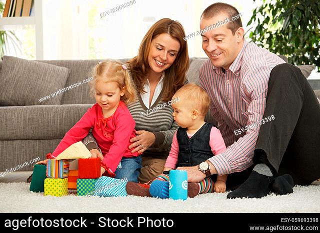 Happy family of four playing on floor in living room sitting on floor in front of sofa