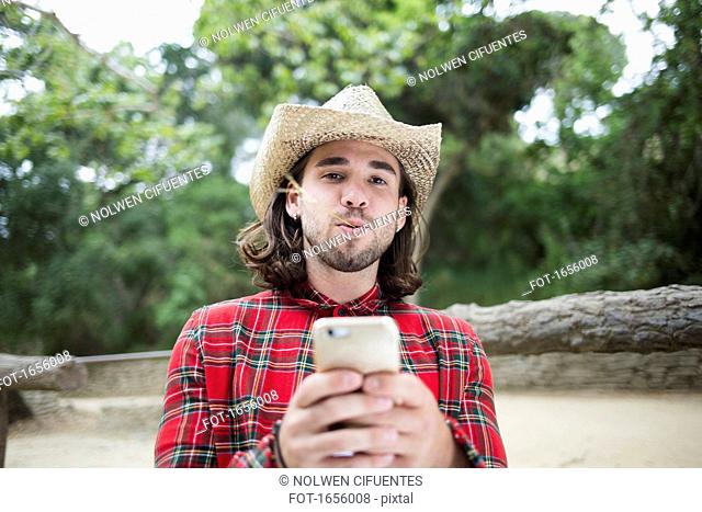 Portrait of man with twig in mouth holding smart phone at park