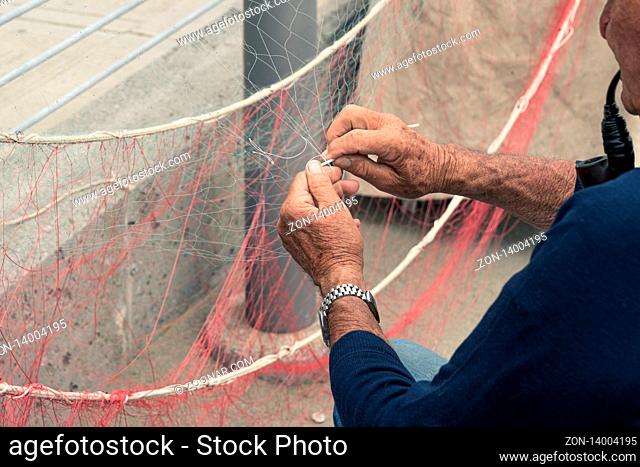 Old fisherman reparing fishing net, sitting with pipe in his mouth