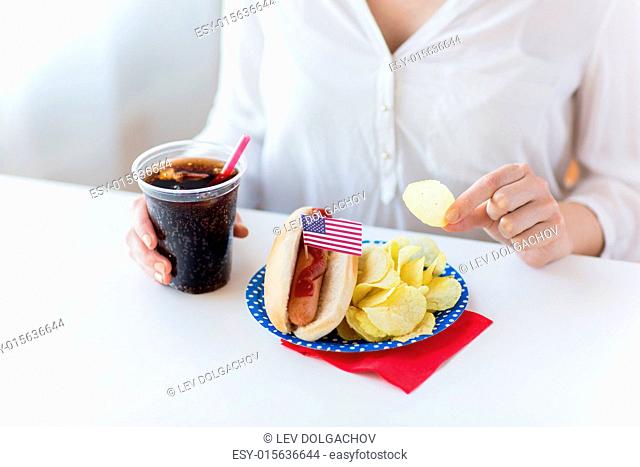 american independence day, celebration, patriotism and holidays concept - close up of woman eating potato chips with hot dog and coca cola in plastic cup on 4th...