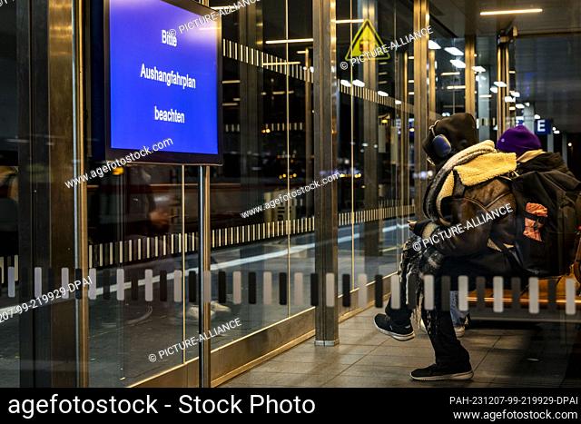 07 December 2023, North Rhine-Westphalia, Duesseldorf: Passengers sit in the waiting area at the main station, a display shows ""Please note the posted...