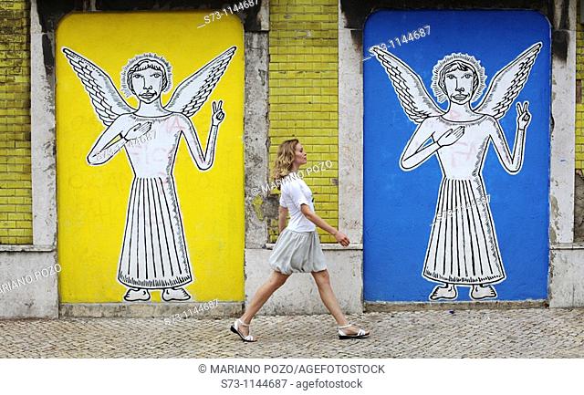 Woman walking near a wall painting with angels in Lisbon streets, Portugal, Europe