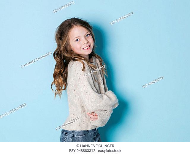 pretty and cool 9 year old girl with brown wool sweater posing in front of blue background in the studio