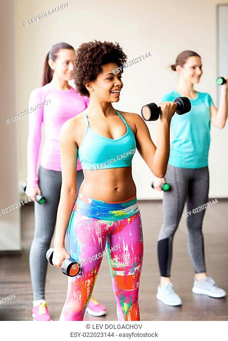 fitness, sport, training and lifestyle concept - group of happy women with dumbbells flexing muscles in gym