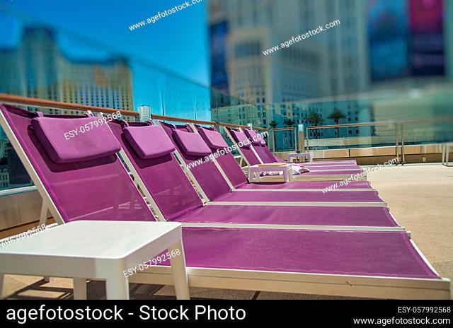 Row of colourful beach deckchairs on a rooftop with city skyline view. Travel, holiday and vacation concept