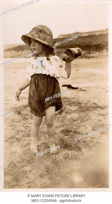 A little girl playing on the beach at an unidentified but fairly remote looking seaside location, c. 1910s/20s