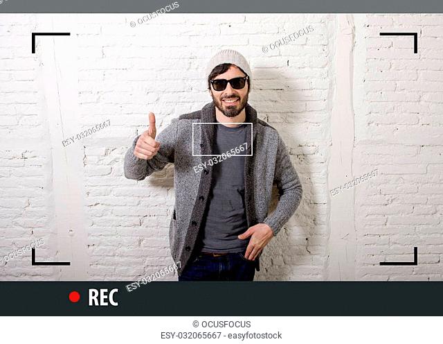 young attractive vlog hipster and trendy style looking man smiling happy talking to camera posing cool with attitude dressing informal in selfie and internet...
