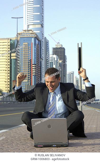 Jubilating businessman with laptop on Shaikh Zayed Road in Dubai