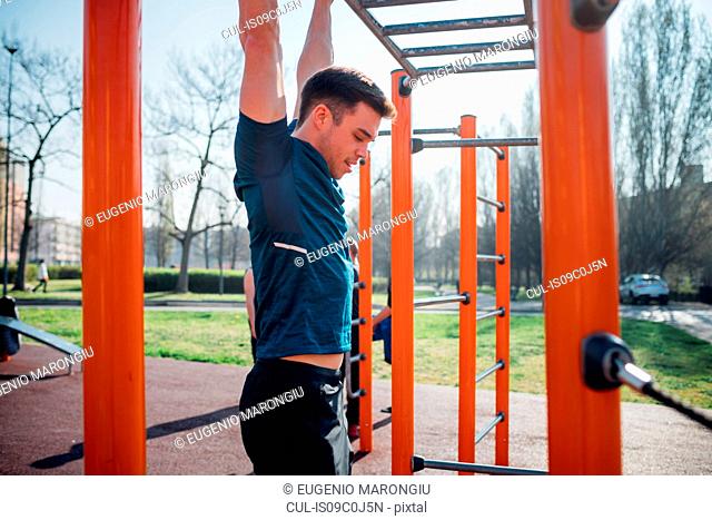 Calisthenics at outdoor gym, young man hanging from exercise equipment