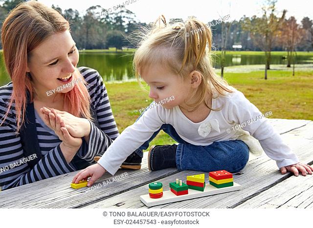 Mother and daughter playing with color shapes game in a park lake