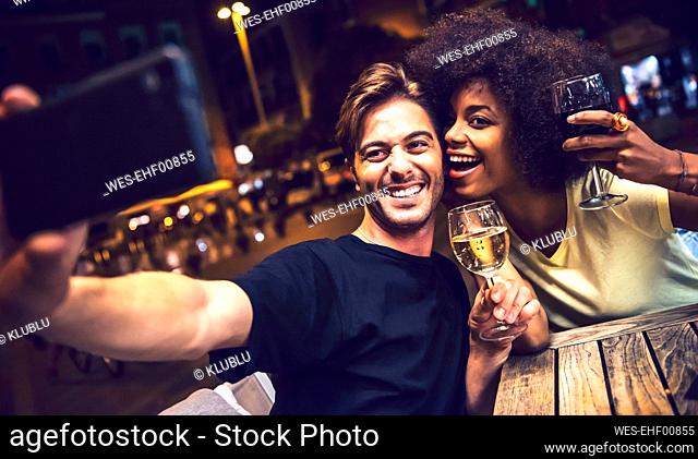 Cheerful couple holding wineglasses taking selfie at date night