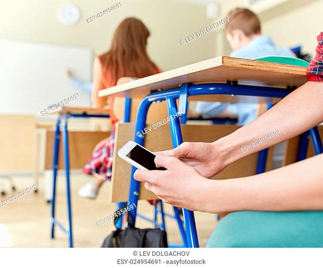education, high school, learning, technology and people concept - student boy hands with smartphone texting on lesson