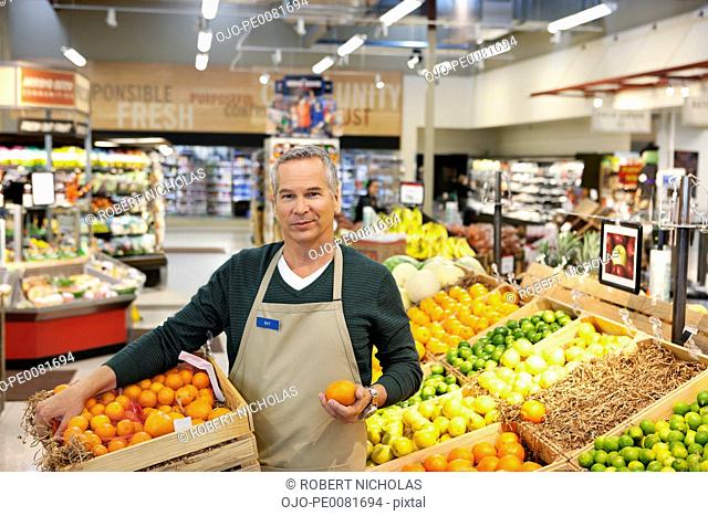 Worker placing oranges in supermarket display