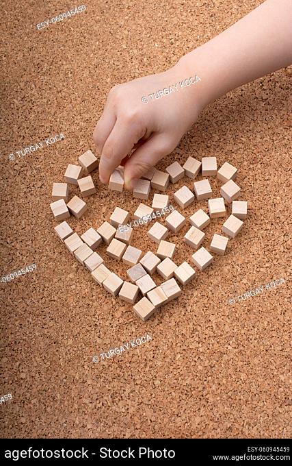 Little wooden cubes form heart shape or valentines day symbol and hand