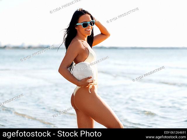 woman in bikini posing with volleyball on beach