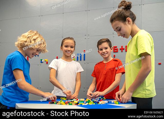 Good moments. Boy and girl smiling at camera playing with friends constructor standing near table in indoor play area