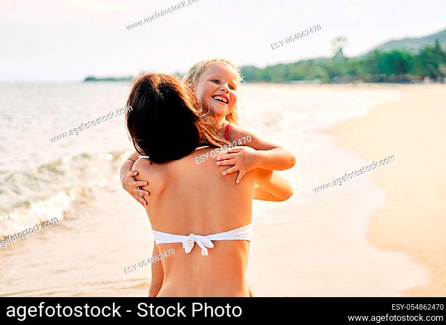 Young woman and her pretty little daughter are hugging and smiling on the tropical beach. Summer vacation, happy family, love concept
