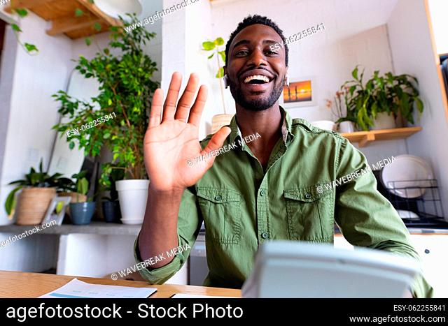 Happy african american man sitting at table in kitchen, having video call